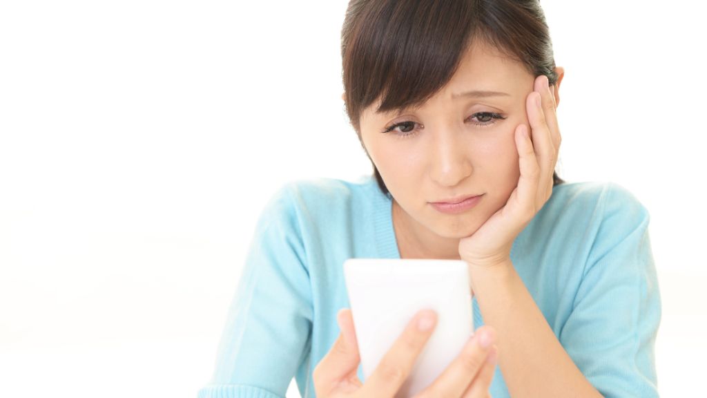 スマートフォンを見ながら悩む女性