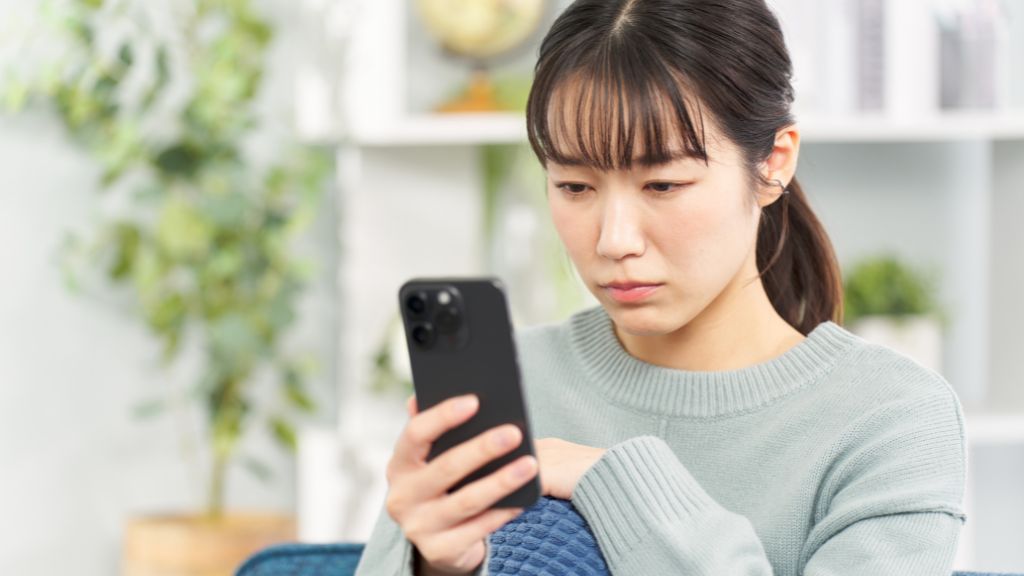 スマホを見つめて悩む女性